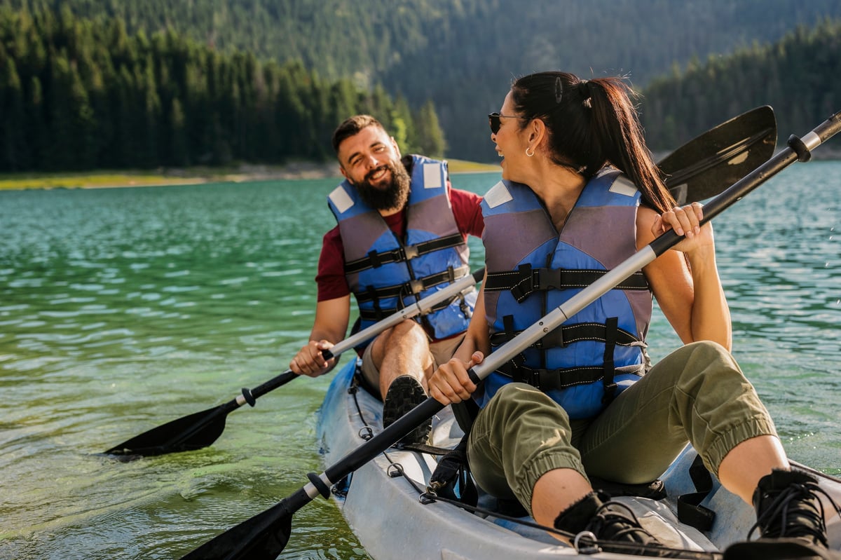 Happy couple wearing life jackets paddles a kayak on a serene mountain lake