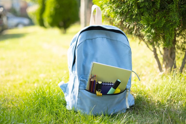 School backpack with stationery on green lawn outdoors. Back to school, education and student lifestyle concept.
