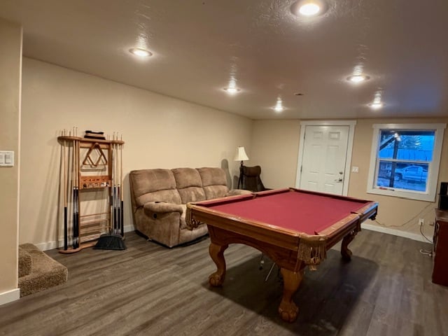 Recreation room with red felt pool table, beige sectional sofa, and wood flooring under recessed ceiling lights