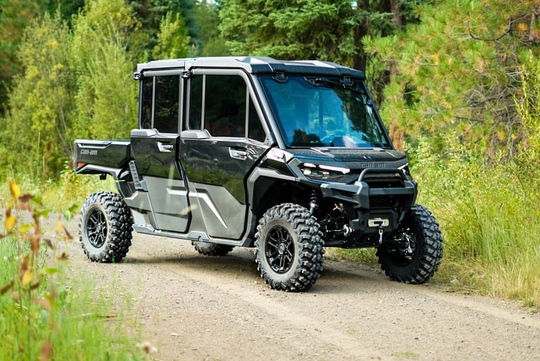 Modern four-seater utility vehicle with large tires parked on a dirt trail surrounded by green trees and vegetation