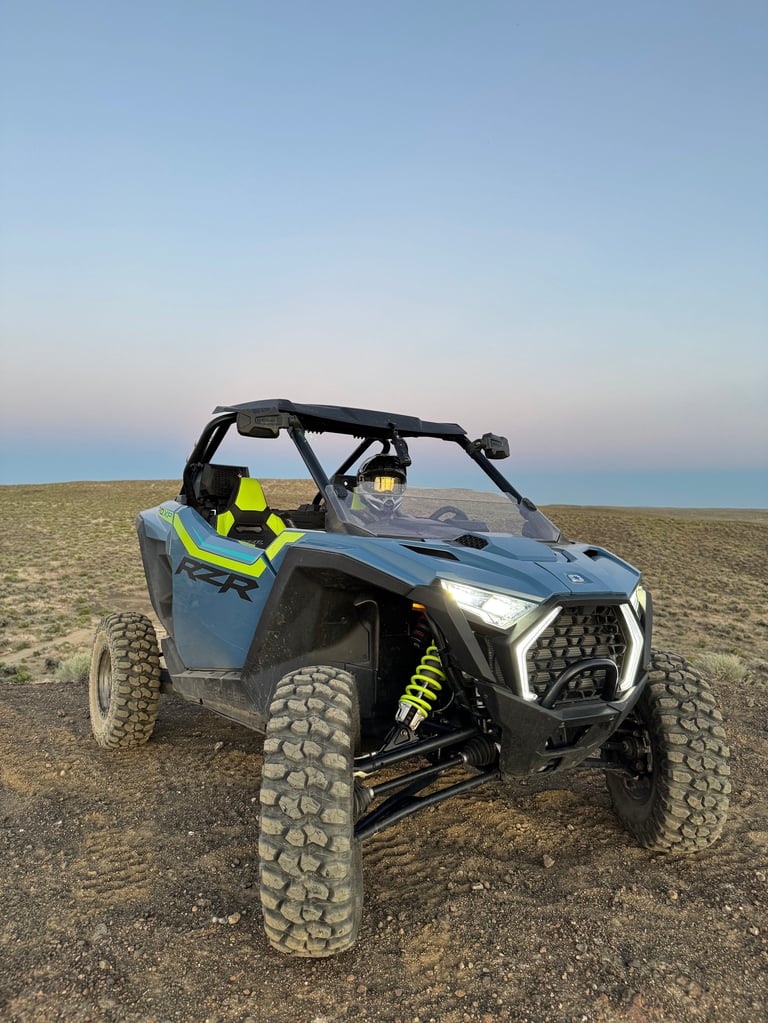 Blue and black side-by-side UTV with yellow safety gear on desert terrain at dusk with clear sky