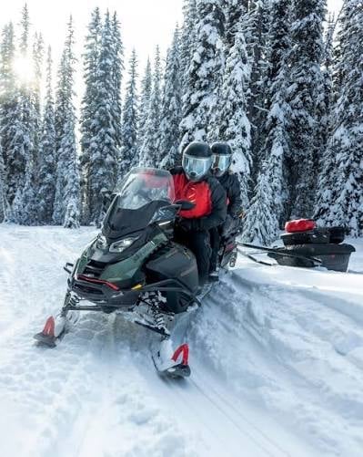 Person in red jacket on black snowmobile with snow-covered evergreen forest in background